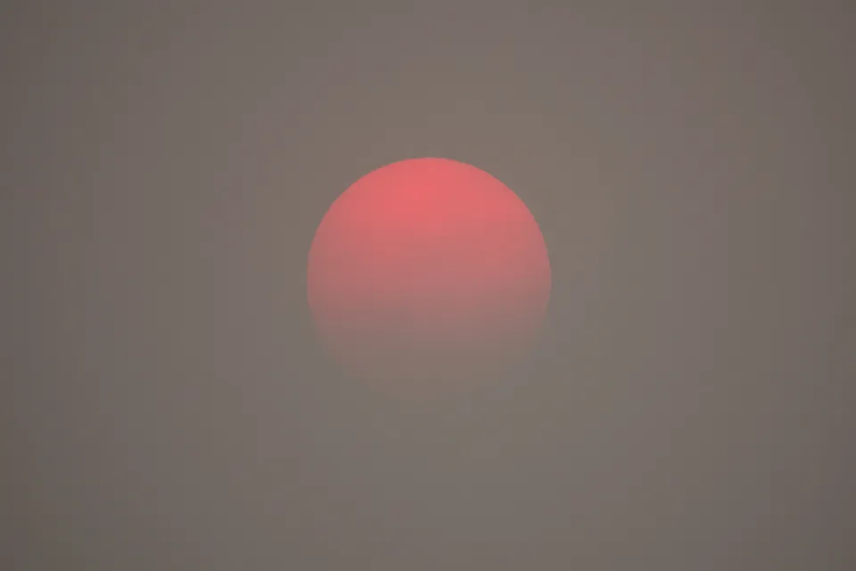 A red sun appears on the horizon, as obscured by haze from wildfire smoke.